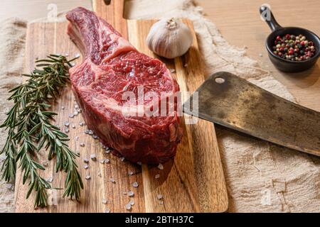 Rohes trockenes Steak Cowboy auf Holzhackbrett rustikalen Stil. Mit Kräutern und Gewürzen und Metzgerspalter Close Up Stockfoto