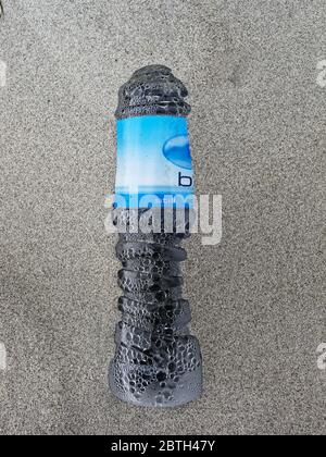 Illustratives Editorial: Plastikflasche aus Flaschenwasser, aufgewaschen und halb im Sand begraben an einem Strand, Westküste, Neuseeland. Stockfoto