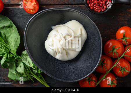 Burrata Handmade Cheese Black Teller serviert mit frischen rohen Tomaten und Basilikumblättern, flachliegend auf dunklem Holzhintergrund, horizontal geschossen Nahaufnahme t Stockfoto
