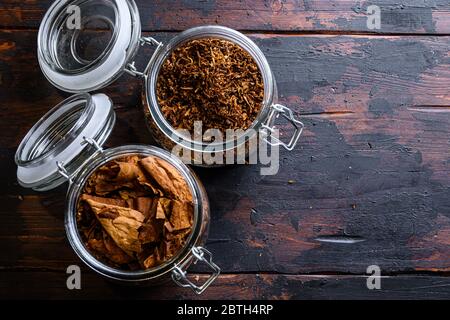 Zigarre und Stapel von Tabakblättern getrockneten Tabaks in Gläsern auf rustikalem Holz dunkle Tabelle Draufsicht Raum für Text. Stockfoto