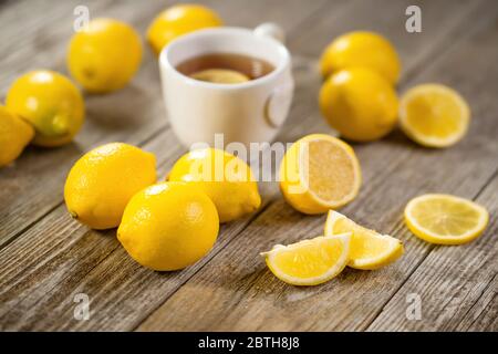 Tasse schwarzer Tee mit Zitronenscheibe und reichlich Zitronen auf grauem Holztisch. Warme Getränke Infusion für kalte Herbst- und Wintertage. Stockfoto