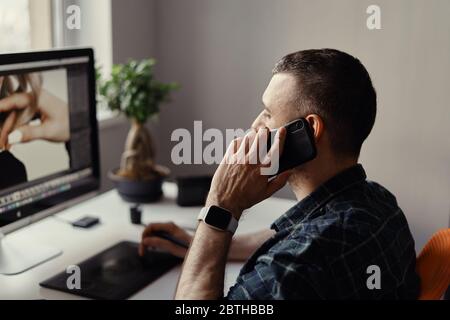 Designer in Freizeitkleidung arbeiten am Computer und Telefonat beim Betrachten des Monitors Stockfoto