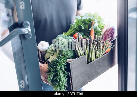 Frische Bio-Gemüse und Gemüse Lieferung. Mann Hände Holding Box mit Landwirt Bio Ernte liefern in der Haustür. Unterstützung für kleine Unternehmen vor Ort Stockfoto