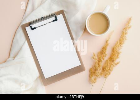 Flach legen leere Papier Clipboard, Tasse Kaffee, weiße Decke und trockene Blumen auf beigem Hintergrund. Schreibtisch für Home Office von oben. Elegant feminin wo Stockfoto