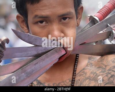 Der Anhänger des thailändischen chinesischen Taoisten durchbohrt während des Vegetarian Festivals in Phuket seine linke Wange mit langen Messern. Stockfoto