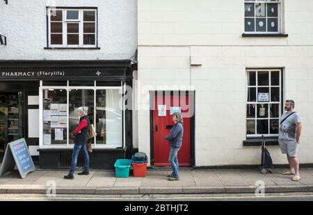 Eine Schlange, die eine sichere soziale Distanz außerhalb der lokalen Apotheke in der kleinen walisischen Stadt Presteigne, Powys, Wales, Großbritannien, aufrecht erhält Stockfoto