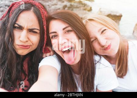 Gruppe glücklicher multirassischer Freunde, die Spaß haben, ein lustiges Selfie mit dem Smartphone zu machen - Beste Freunde, die ein Foto mit dem Meer im Hintergrund machen - Fr Stockfoto