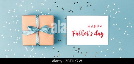 Geschenkbox gebunden blaues Band und Happy Father's Day Grußkarte auf blauem Hintergrund mit Konfetti verziert. Blick von oben, Urlaubskonzept. Stockfoto