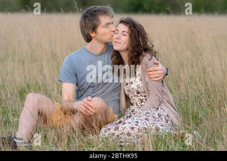 Ein junges attraktives schönes Paar lächelt zusammen in einem schönen Außenfeld zeigt ihre Liebe zueinander und küssen Stockfoto