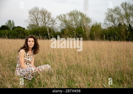 Eine schöne und gesunde junge Frau im Kleid tanzt friedlich meditierend und denkend in einem braunen Grasfeld bei Sonnenuntergang Stockfoto