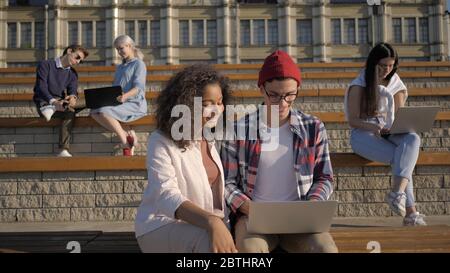 Studierende, die Projekte auf Laptops außerhalb der Universität machen. Stockfoto