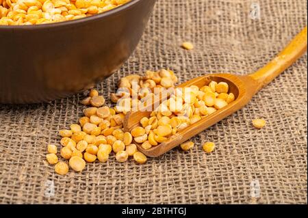 Gelbe Erbsen in einem Holzlöffel auf einem Hintergrund von Burlap mit einer rauen Textur gespalten. Traditionelles Getreide für die Herstellung von Suppen und Porridge. Nahaufnahme Stockfoto