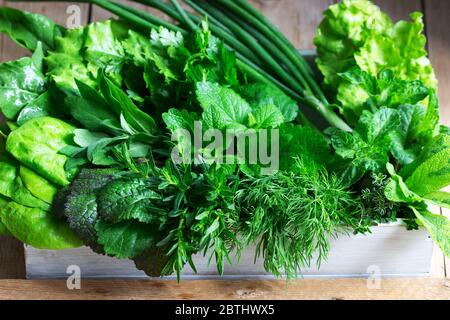 Eine Vielzahl von würzigen Kräutern, Salat und grünen Zwiebeln auf einem hölzernen Hintergrund. Rustikaler Stil. Stockfoto