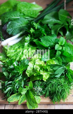 Eine Vielzahl von würzigen Kräutern, Salat und grünen Zwiebeln auf einem hölzernen Hintergrund. Rustikaler Stil. Stockfoto