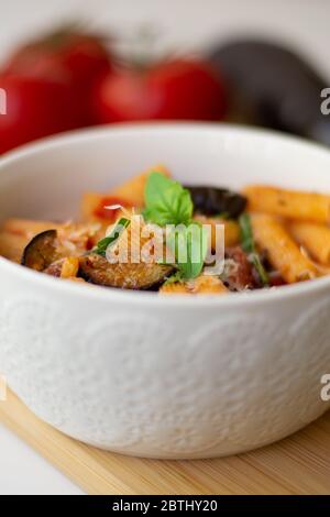 Traditionelles italienisches Gericht: Pasta alla norma mit Tomaten, Auberginen, Knoblauch, Basilikum und Ricotta auf einem Holzbrett Stockfoto