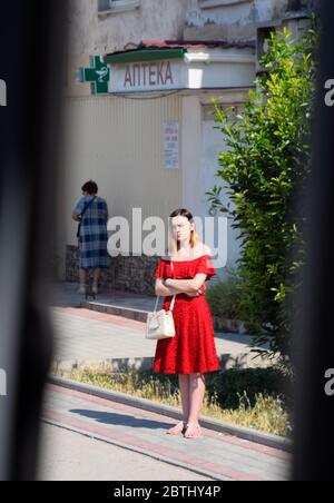 Balaklava, Republik Krim - 9. Juni 2019: Ein Mädchen in einem roten Kleid wartet auf einen Bus am Straßenrand. Stockfoto