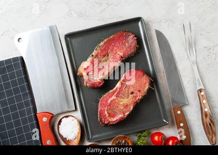 Marinierte rohe Steaks auf Steintisch mit Gewürzen Stockfoto