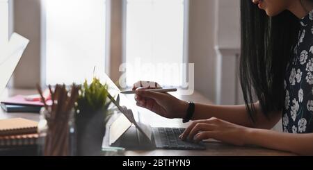 Zugeschnittenes Bild von schönen Frau skizziert auf Computer-Tablet mit einem Stift und sitzen am hölzernen Schreibtisch über komfortablen Wohn Roo Stockfoto