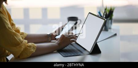 Foto von stilvollen Frau mit einem Smartphone und Stift in den Händen während vor ihrem Computer-Tablet mit Tastatur-Fall, die auf whit setzen sitzen Stockfoto