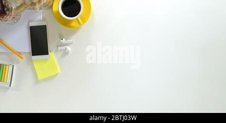 Büroschreibtisch mit Smartphone auf weißem Schreibtisch, der von Computer-Laptop, Tablet, Wildgras, Stift, schnurlosem Ohrhörer, Kaffeetasse umgeben ist, Stockfoto