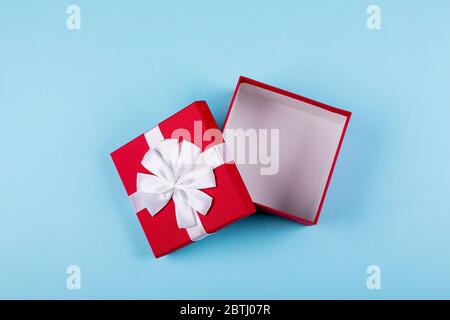 Öffnen Sie die rote Geschenkbox auf blauem Papierhintergrund. Draufsicht, flaches Lay, Platz für Objekt. Modell, Urlaubskonzept. Stockfoto