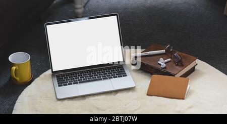 Foto von weißen leeren Bildschirm Computer setzen auf weißen pelzigen Teppich und umgeben von Notebook, Bücher, Kaffeetasse, Stift, Brille und schnurlose Kopfhörer Stockfoto