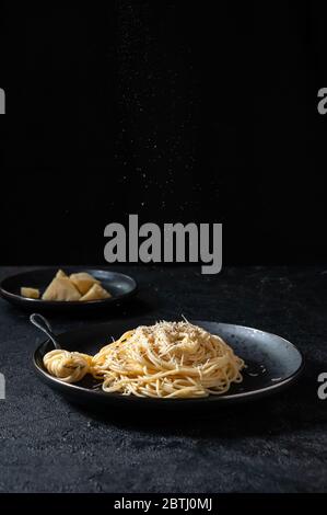 Cacio e Pepe - Italienische Pasta mit Käse und Pfeffer auf schwarzem Teller auf dunklem Hintergrund. Stockfoto