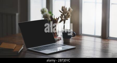 Laptop auf Holzschreibtisch setzen und umgeben von Stapel Notizbuch, Bleistifthalter, Wildgras in Vase, Topfblumen und Kaffeetasse. Stockfoto