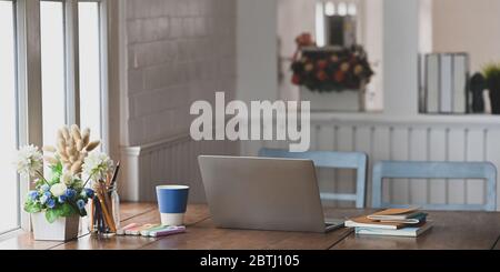 Computer-Laptop, dass auf Holz Schreibtisch, der von Stapel von Büchern, Topfe von Blumen, Wildgras, Bleistifthalter, Kaffeetasse und ma umgeben setzen Stockfoto