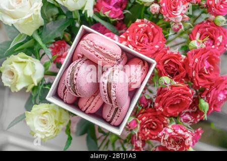 Zarte Himbeer-Makronen auf dem Tisch mit einem Bouquet aus Scharlach und weißen Rosen. Nahaufnahme. Selektiver Fokus. Stockfoto