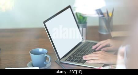 Cropped Bild der schönen Frau auf weißen leeren Bildschirm Computer-Laptop, dass auf Holz Schreibtisch setzen von Topfpflanze umgeben, Bleistift h tippen Stockfoto