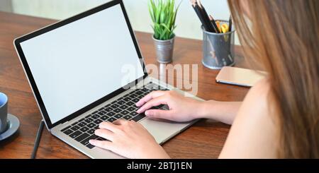 Cropped von schönen Frau auf weißen leeren Bildschirm Computer-Laptop, dass auf Holz Schreibtisch setzen von Topfpflanze umgeben, Bleistifthalter tippen Stockfoto