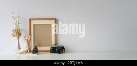 Kamera mit Objektiv auf dem Schreibtisch des Fotografen, der von einem Kegel aus Kiefernholz umgeben ist, einem Stapel Notizbuch, einem leeren Bilderrahmen, Bleistiften in Glasvase und wildem Gra Stockfoto