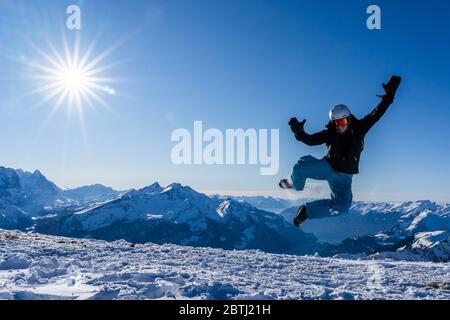 Mädchen mit Brille und Helm springt im Winter in der Luft. Blauer Himmel und strahlender Sonnenschein auf den Bergen der Schweiz. Konzept. Stockfoto