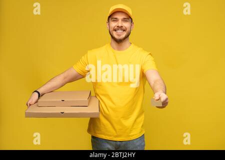 Porträt des jungen Liefermanns in gelber Uniform mit Pizzakartons isoliert auf gelbem Hintergrund. Stockfoto