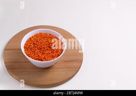 Orangefarbene Linsen in einer weißen Schüssel auf einem runden Schneidebrett. Gesundes Essen Konzept. Kopierbereich. Stockfoto