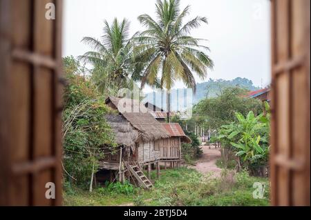 Blick durch ein Fenster zu den anderen Häusern in einem kleinen Dorf in der Nähe des Mekong Flusses, Nord-Laos, Südostasien Stockfoto