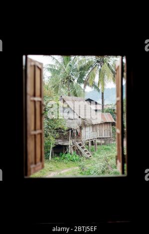 Blick durch ein Fenster zu den anderen Häusern in einem kleinen Dorf in der Nähe des Mekong Flusses, Nord-Laos, Südostasien Stockfoto