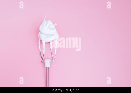 Schlagen Sie auf dem Mixer das Eiweiß auf einem rosa Hintergrund Stockfoto