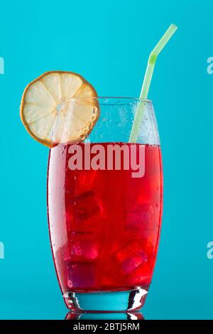 Ein Glas alkoholfreies Getränk mit viel Eis, einer Scheibe Zitrone und einem Stroh auf blauem Hintergrund Stockfoto