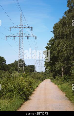 Übertragungsleitung oder Oberleitung Stromkabel mit Strommasten entlang ländlichen Feldweg Landstraße Weg durch die deutsche Landschaft Stockfoto