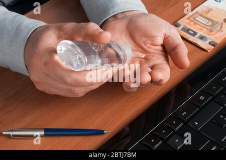 Bankangestellten desinfizieren seine Hände mit einem Desinfektionsgel, bevor sie die Banknoten berühren Stockfoto