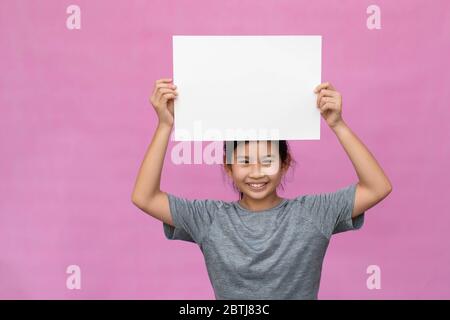 Kleine asiatische Mädchen mit weißem Papier isoliert auf rosa Hintergrund. Stockfoto