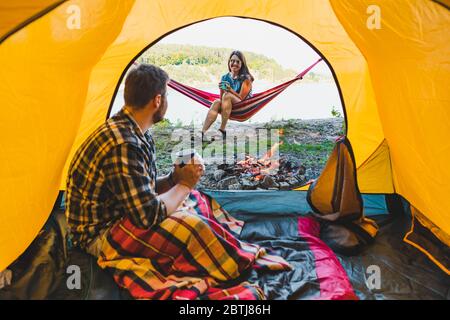 Pärchen ruht in der Nähe des Feuers. Mann sitzt im Zelt Frau auf Hängematte Stockfoto