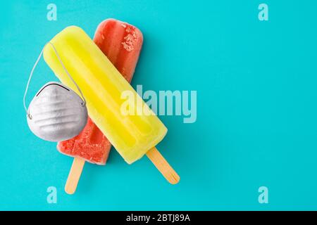 Zitronen- und Erdbeerpopsicles mit schützender Gesichtsmaske auf blauem Hintergrund Stockfoto