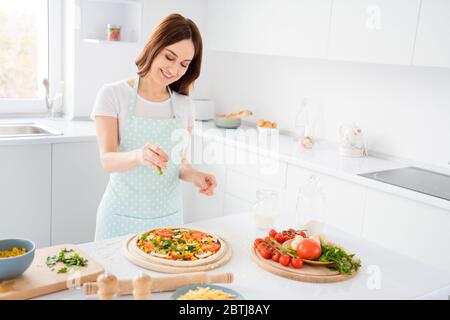 Foto von schönen fröhlichen Hausfrau genießen Hobby Kochen Familienrezept Abendessen Pizza fügen Sie letzte Zutat vor dem Einlegen in Ofen tragen T-Shirt Stockfoto