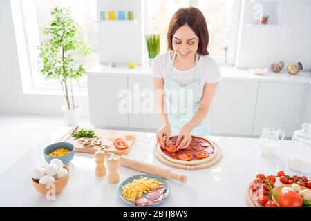 Top über hohen Winkel Ansicht Foto von positiven fröhliche Hausfrau genießen Kochen italienische margarita Pizza setzen Salami Rindfleisch Schweinefleisch Tomatenscheiben tragen gepunktet Stockfoto