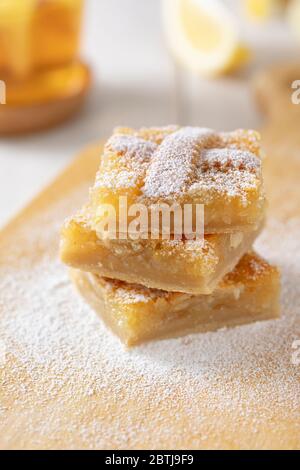 Drei Stücke von hausgemachten Mürmelade Zitronenkuchen mit Puderzucker bestreut. Tee in einem Becher und Zitronenscheiben im Hintergrund. Nahaufnahme Stockfoto