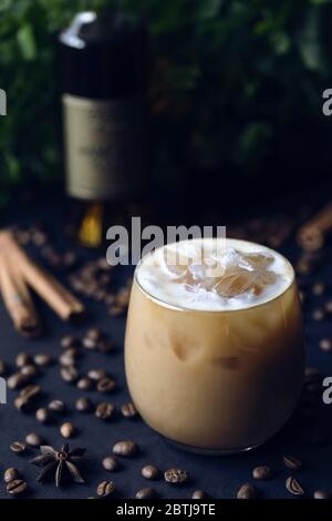Kalter würziger Kaffee-Cocktail mit Eis auf dunklem Hintergrund mit Cognac-Flasche, Kaffeebohnen, Anisstern und Zimtstangen Stockfoto