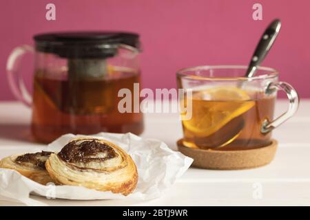 Hausgemachte Blätterteig Zimtbrötchen serviert mit schwarzem Tee mit Zitrone als Frühstück. Stockfoto